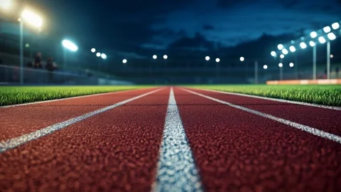 View of a well-lit athletic track at night, showcasing vibrant red surface and Stock Footage 302429213
