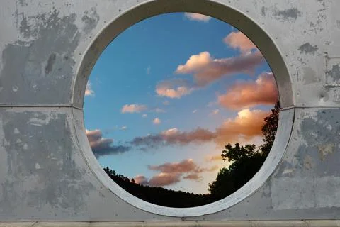 View of white clouds in sunset sky through hole in concrete wall Stock Photos