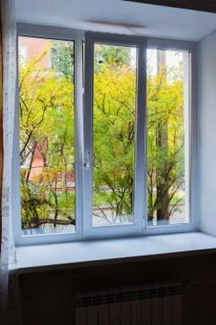 View from a white plastic window on green trees and a red house Stock Photos