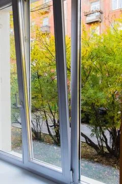 View from a white plastic window on green trees and a red house Stock Photos