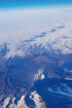 View from window of plane to blue sky and snowy mountain peaks in white clouds Stock Photos