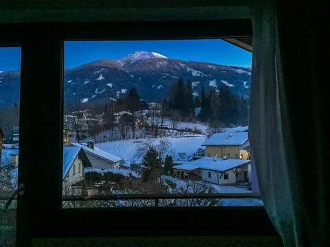 View from window to snow-capped mountain peaks and alpine village in evening Stock Photos