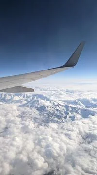 View from the window on the wing of the plane, blue sky, clouds and mountains Stock Photos