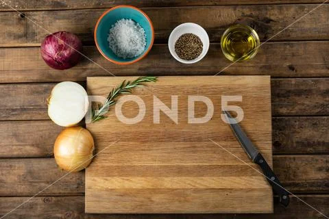 View of a wooden cutting board and knife with onion and seasonings arranged on a Stock-Fotos