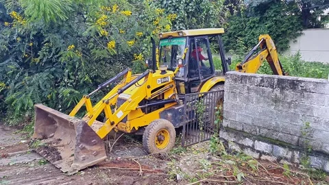 View of Yellow JCB clearing grass near compound wall in outdoor maintenance.. Vídeo Stock 332908486