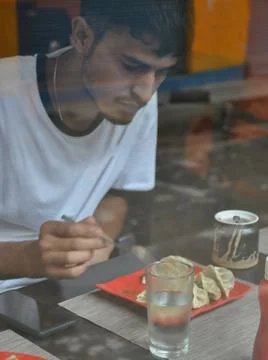 View of a young guy eating fast food in the cafe seen through the window glass.  Stock Photos