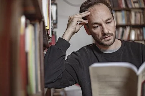 View of a young guy sitting alone and reading vintage books in a library, Lis Stock Photos