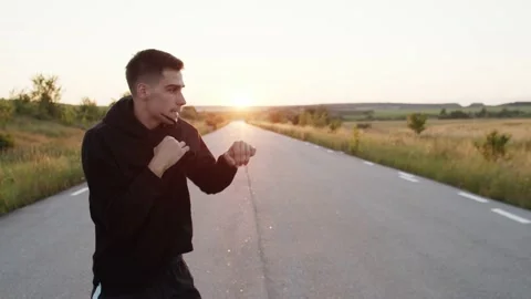 View of young kickboxer training kicks on country road singly during sunset Video stock 140263682