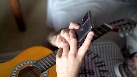 View of young man with guitar lying on a sofa and using a mobile phone Stock Footage 162169289