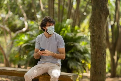 View of young man using a smartphone at day time with a green park in the bac Stock Photos