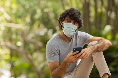 View of young man using a smartphone at day time with a green park in the bac Stock Photos