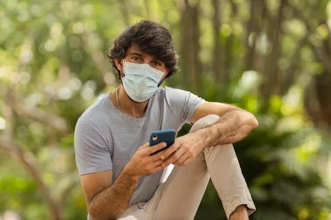 View of young man using a smartphone at day time with a green park in the bac Stock Photos