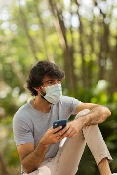 View of young man using a smartphone at day time with a green park in the bac Stock Photos
