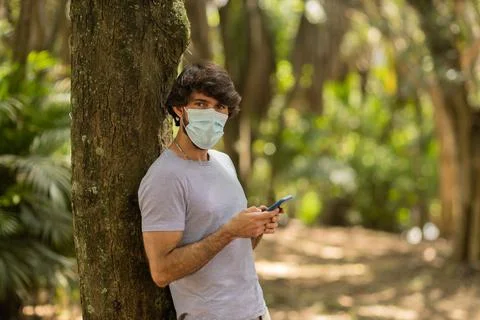 View of young man using a smartphone at day time with a green park in the bac Stock Photos