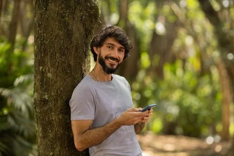 View of young man using a smartphone at day time with a green park in the bac Stock Photos