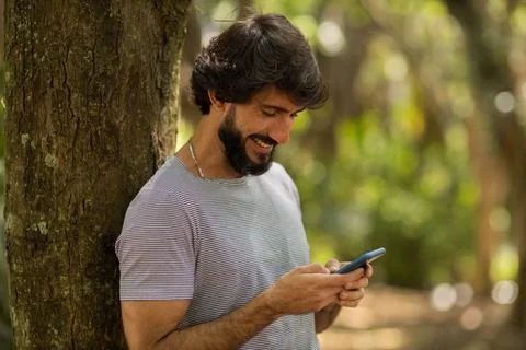 View of young man using a smartphone at day time with a green park in the bac Stock Photos