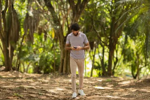 View of young man using a smartphone at day time with a green park in the bac Stock Photos
