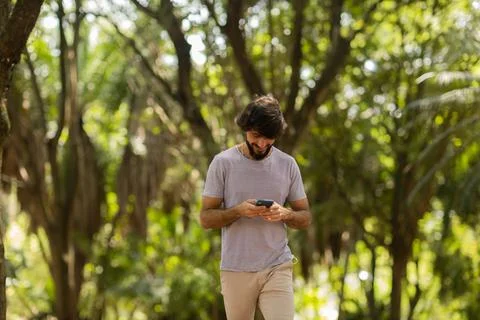 View of young man using a smartphone at day time with a green park in the bac Stock Photos