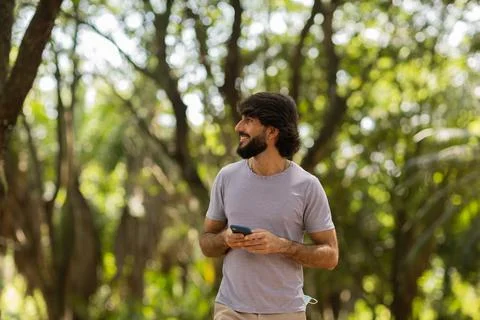 View of young man using a smartphone at day time with a green park in the bac Stock Photos