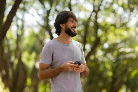 View of young man using a smartphone at day time with a green park in the bac Stock Photos