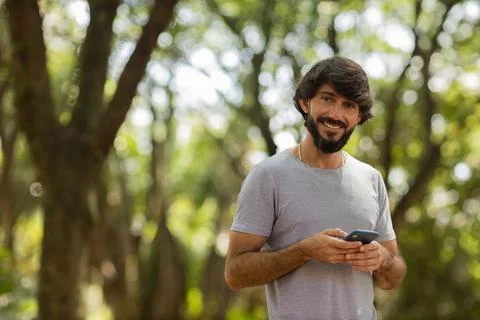 View of young man using a smartphone at day time with a green park in the bac Stock Photos