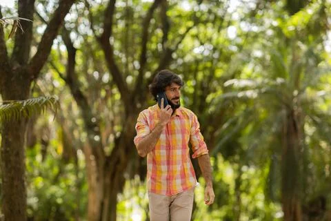 View of young man using a smartphone at day time with a green park in the bac Stock Photos