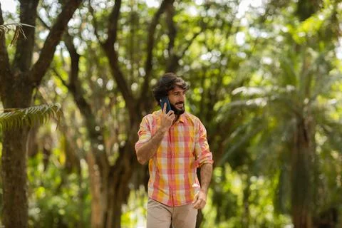 View of young man using a smartphone at day time with a green park in the bac Stock Photos