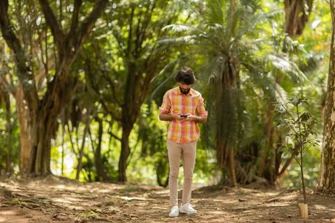 View of young man using a smartphone at day time with a green park in the bac Stock Photos