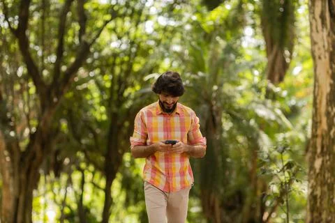 View of young man using a smartphone at day time with a green park in the bac Stock Photos