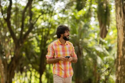 View of young man using a smartphone at day time with a green park in the bac Stock Photos