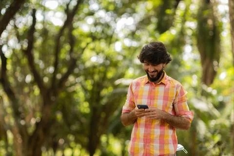 View of young man using a smartphone at day time with a green park in the bac Stock Photos