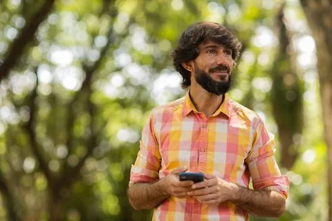 View of young man using a smartphone at day time with a green park in the bac Stock Photos
