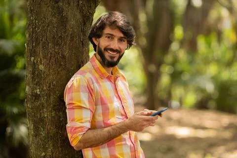 View of young man using a smartphone at day time with a green park in the bac Stock Photos
