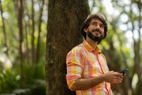 View of young man using a smartphone at day time with a green park in the bac Stock Photos