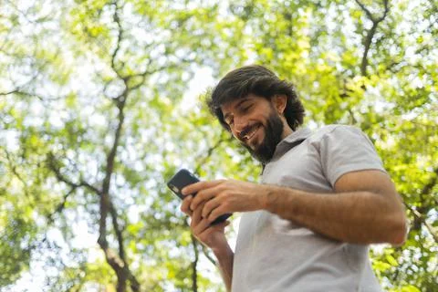 View of young man using a smartphone at day time with a green park in the bac Stock Photos