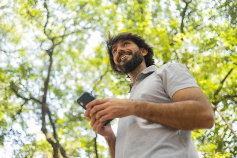View of young man using a smartphone at day time with a green park in the bac Stock Photos