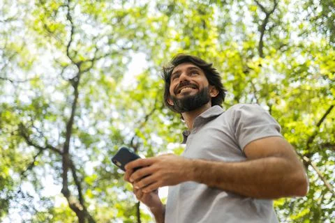 View of young man using a smartphone at day time with a green park in the bac Stock Photos