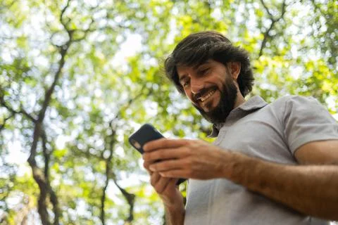 View of young man using a smartphone at day time with a green park in the bac Stock Photos