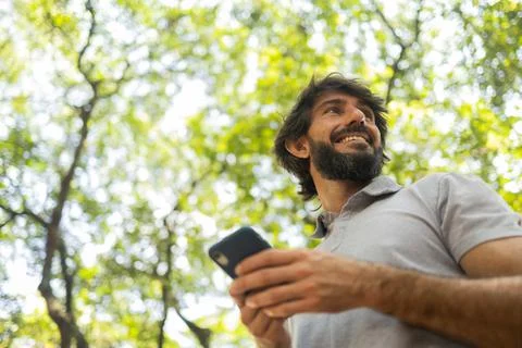 View of young man using a smartphone at day time with a green park in the bac Stock Photos