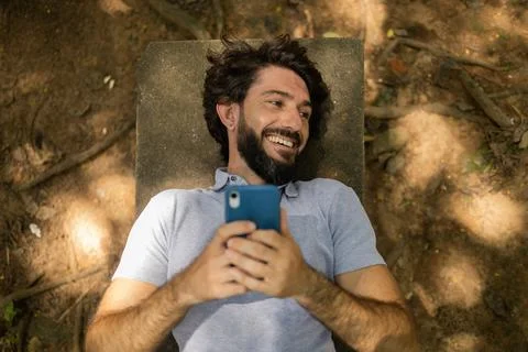 View of young man using a smartphone at day time lying down on a bench at a p Stock Photos