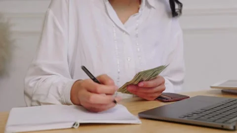 View of young woman sits while counts dollar money at table. Woman calculat.. Stock Footage 266470387
