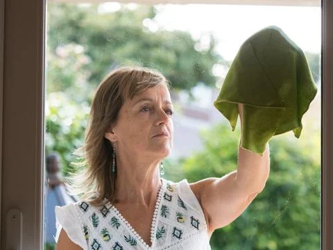 Viewed from inside a lady cleans the outside of a glass door with a green cloth. Stock Photos