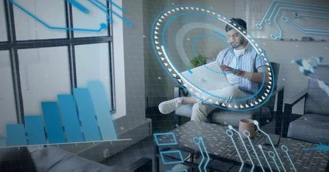 Viewing AR interface Indian man holding smartphone on gray sofa in modern office Stock Photos