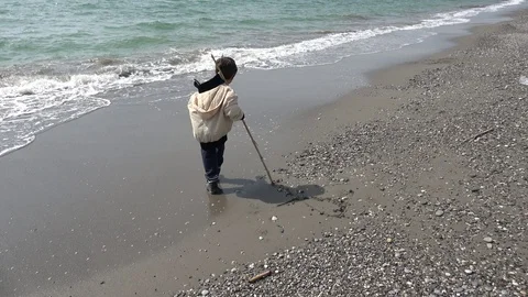 Viewing a child drawing with a stick on sandy beach near the stormy sea Video stock 127897443
