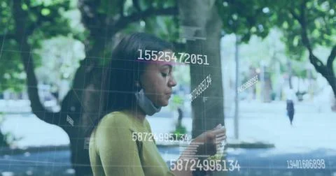 Viewing grid numeric data on smartphone on tree-lined path wearing mustard top 스톡 사진