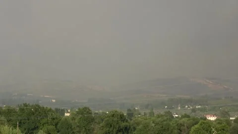 Viewing heavy smoke from wildfire rising over mountain forest and village 動画素材 342257894