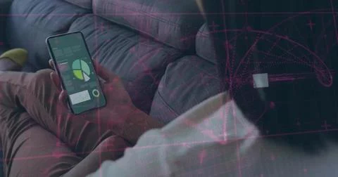 Viewing smartphone data sitting on grey sofa wearing white shirt and beige pants Foto stock