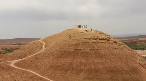 Viewpoint. Distant figures stand atop a vast, dry, earthy hill Stock Photos