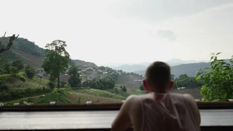 Views of a boy sitting looking at his phone in front of a hillside full of Stock Footage 221723227