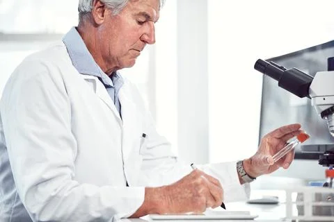 This vile seems a bit different. a focused elderly male scientist holding up a Stock Photos